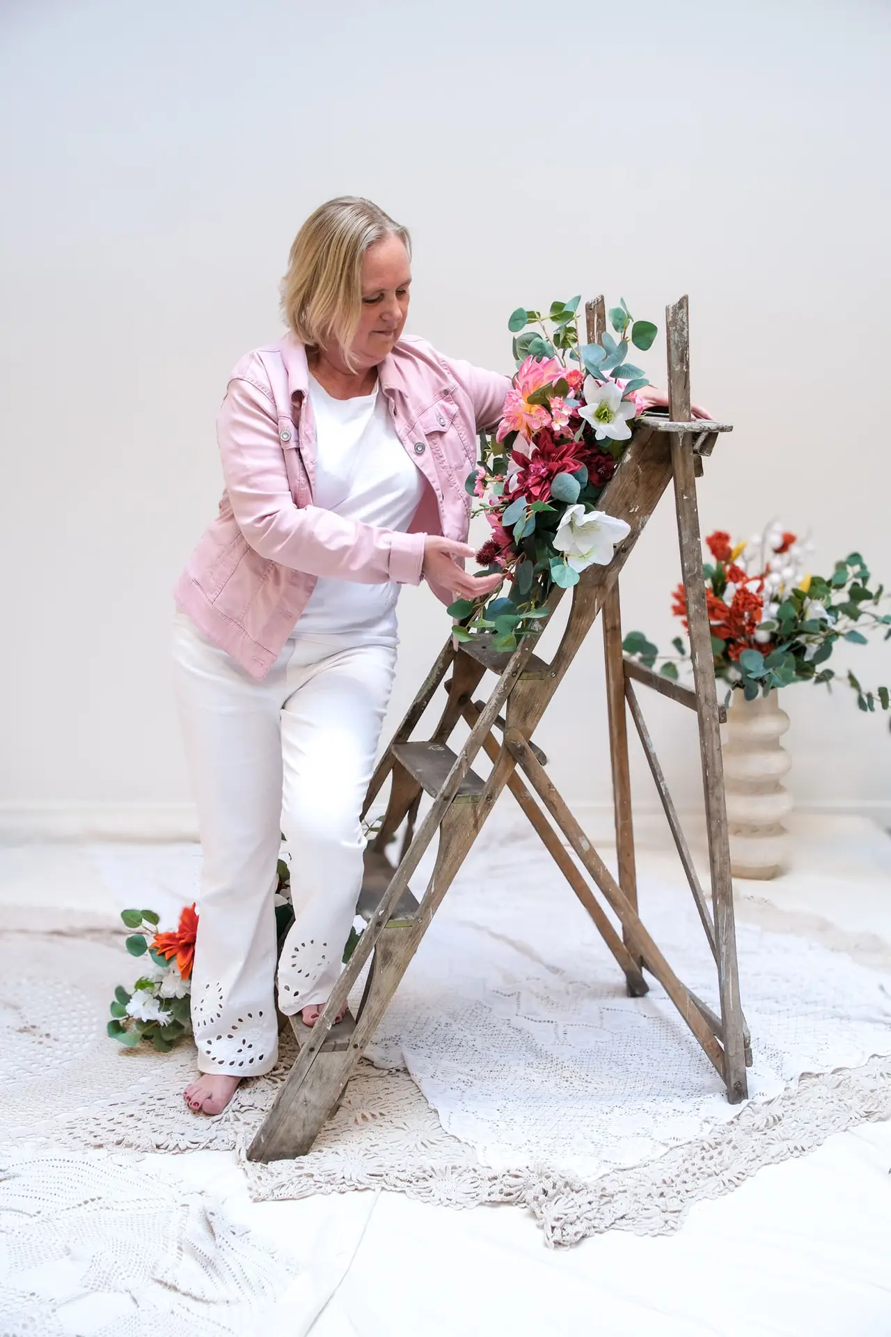 Anja Van Damme leunt tegen een houten ladder met bloemen