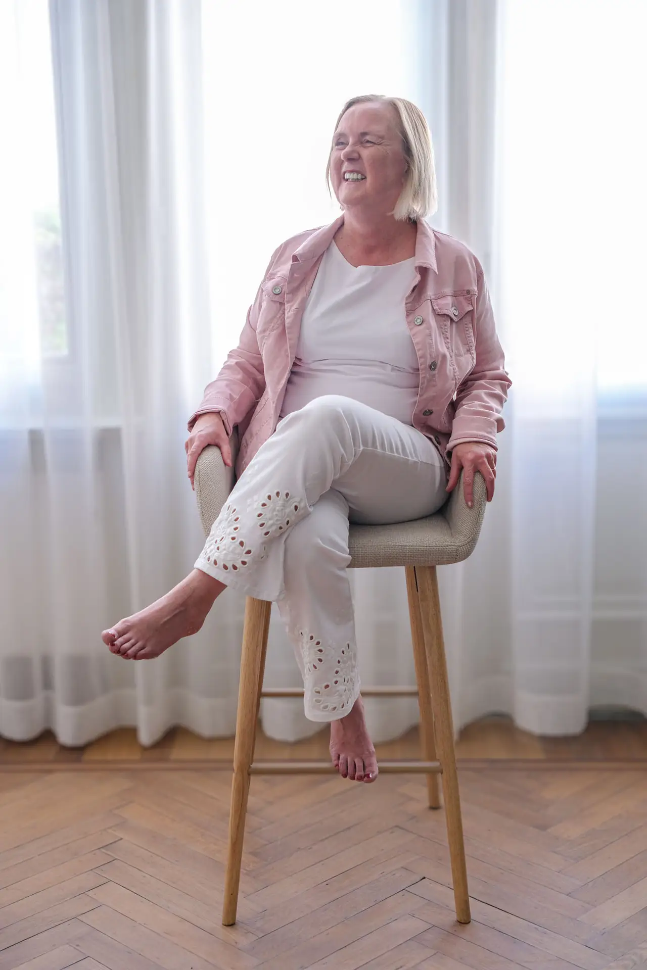 Anja Van Damme zit op een barkruk voor het raam