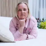 Anja Van Damme zit ontspannen op een wit bed