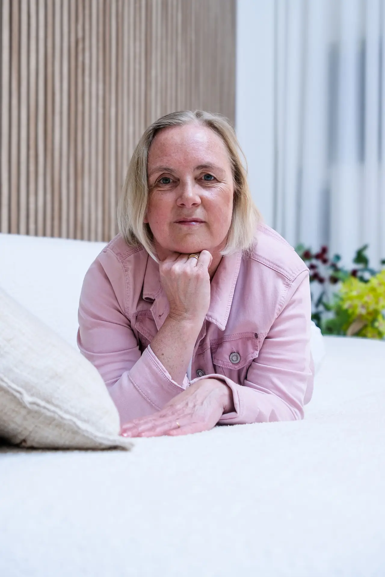 Anja Van Damme zit ontspannen op een wit bed